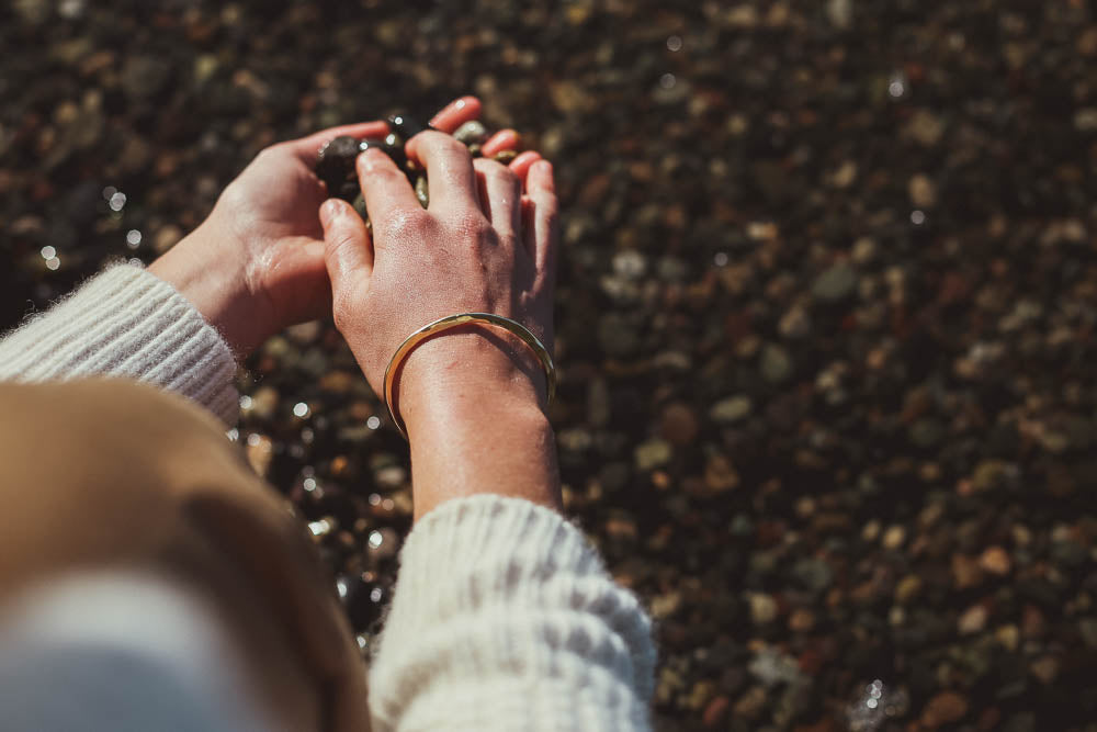 Hands holding pebbles model wearing brass bracelet